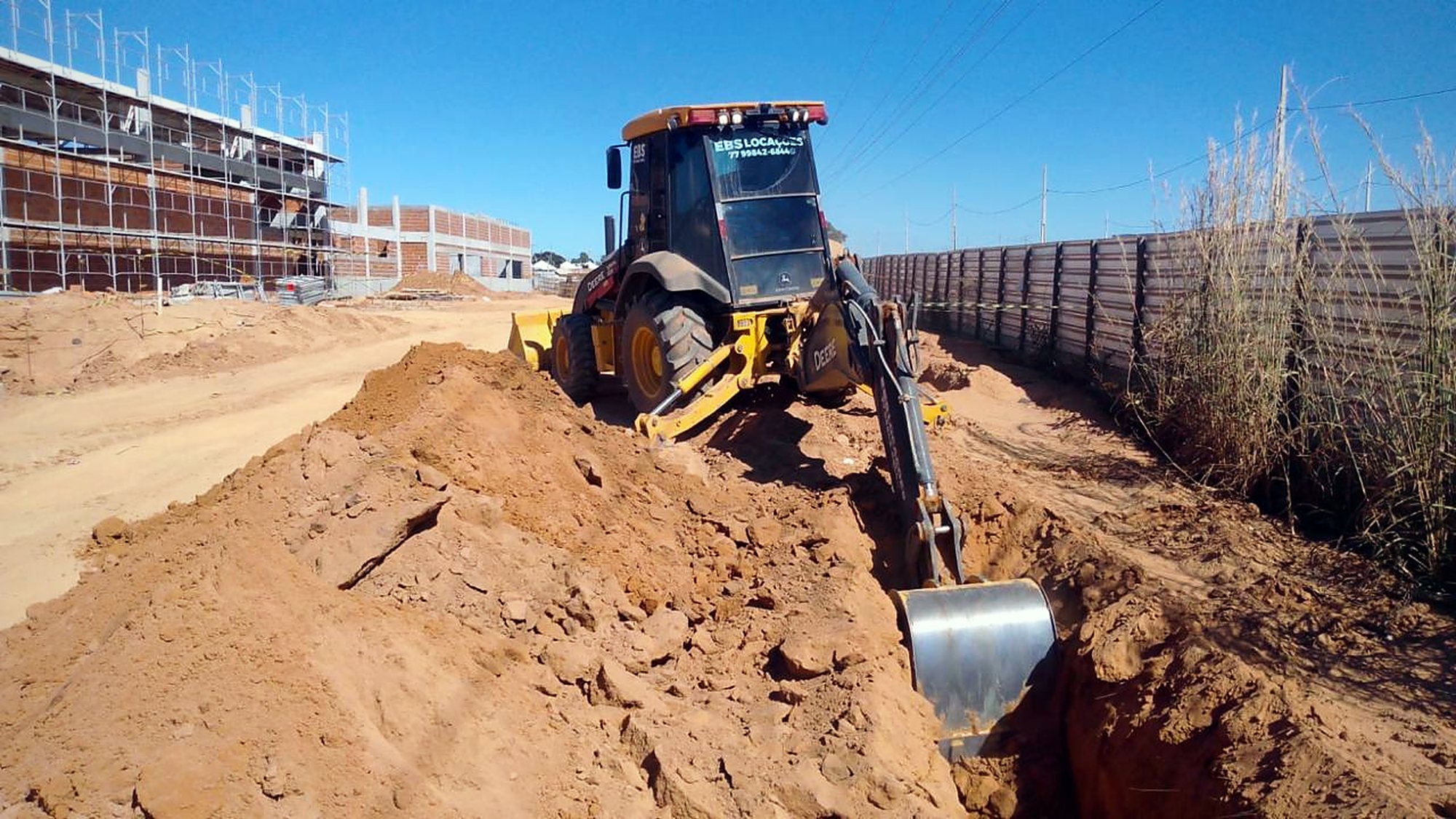 Escavadeira nivela terreno junto à edificação em obra do complexo