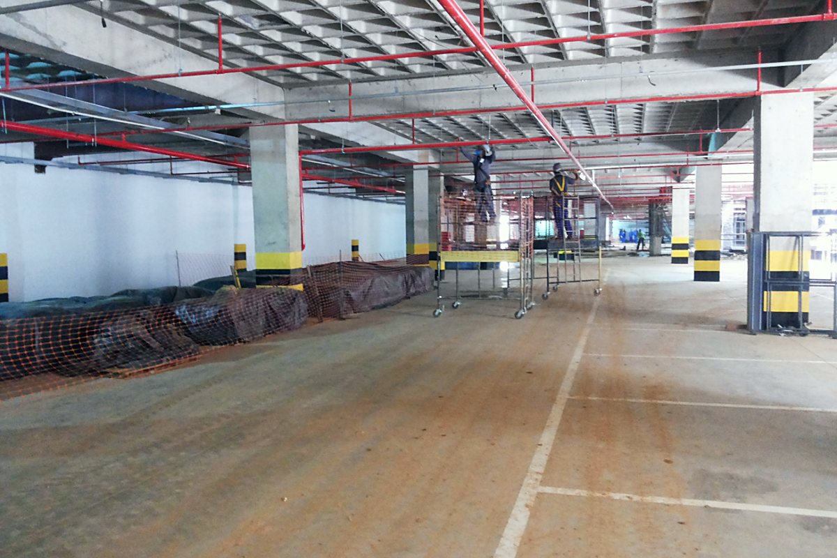 Estacionamento coberto em obra, com rede de incêndio e infraestrutura elétrica aparentes
