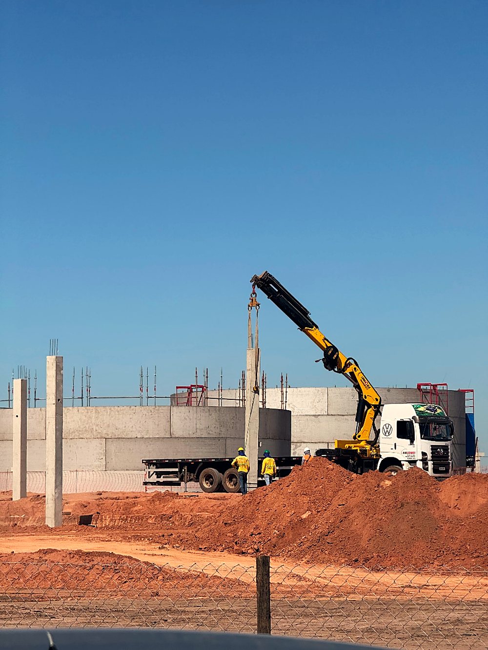 Caminhão munck posicionando poste em frente de obra com solo em terraplenagem