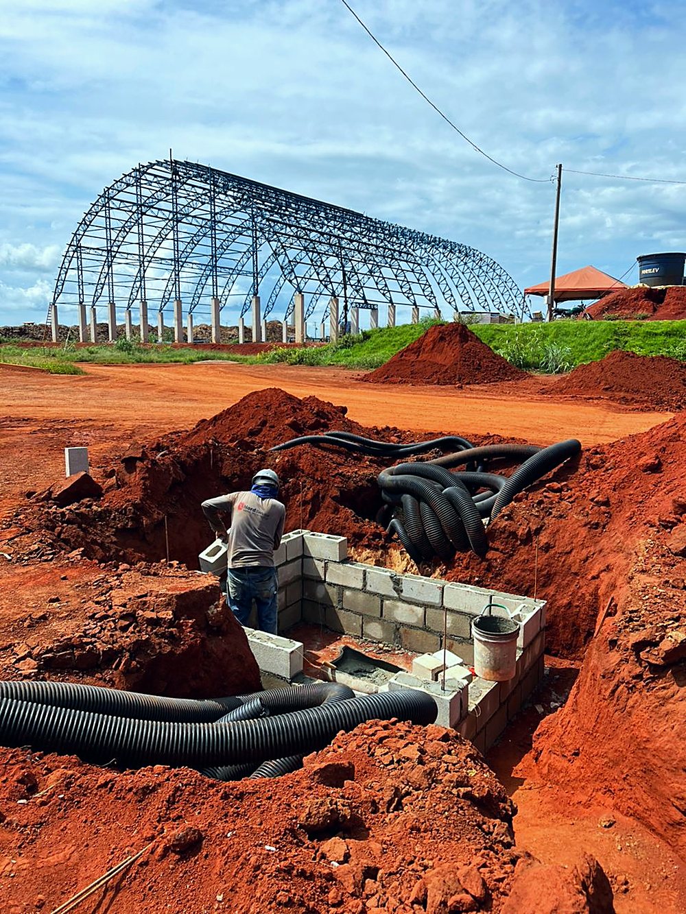 Estrutura metálica em arco do galpão e vala de infraestrutura elétrica em primeiro plano