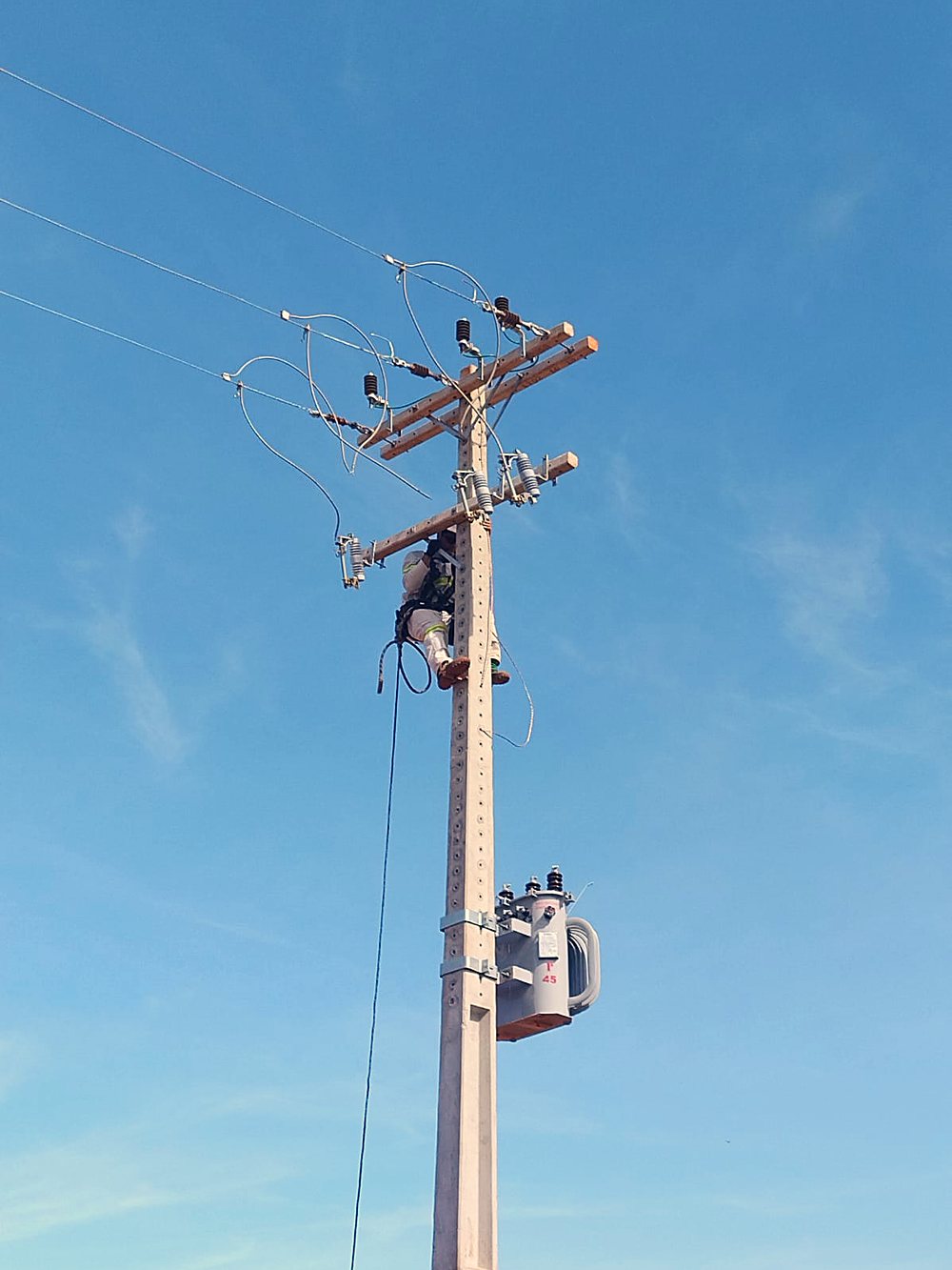 Poste de rede de média tensão com transformador e chaves, visto de baixo contra o céu