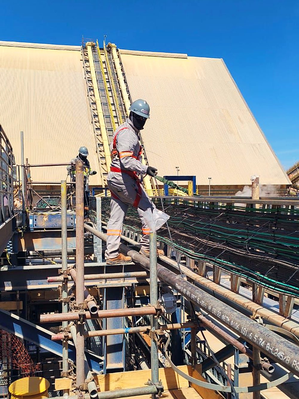 Trabalhador sobre passarela de correia transportadora em estrutura industrial