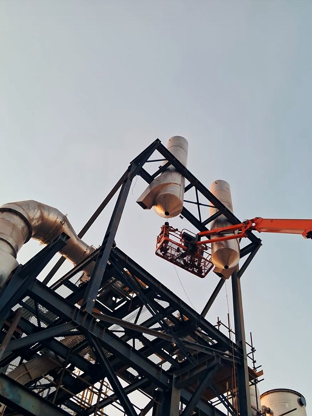 Estrutura metálica industrial em montagem, vista de baixo contra o céu