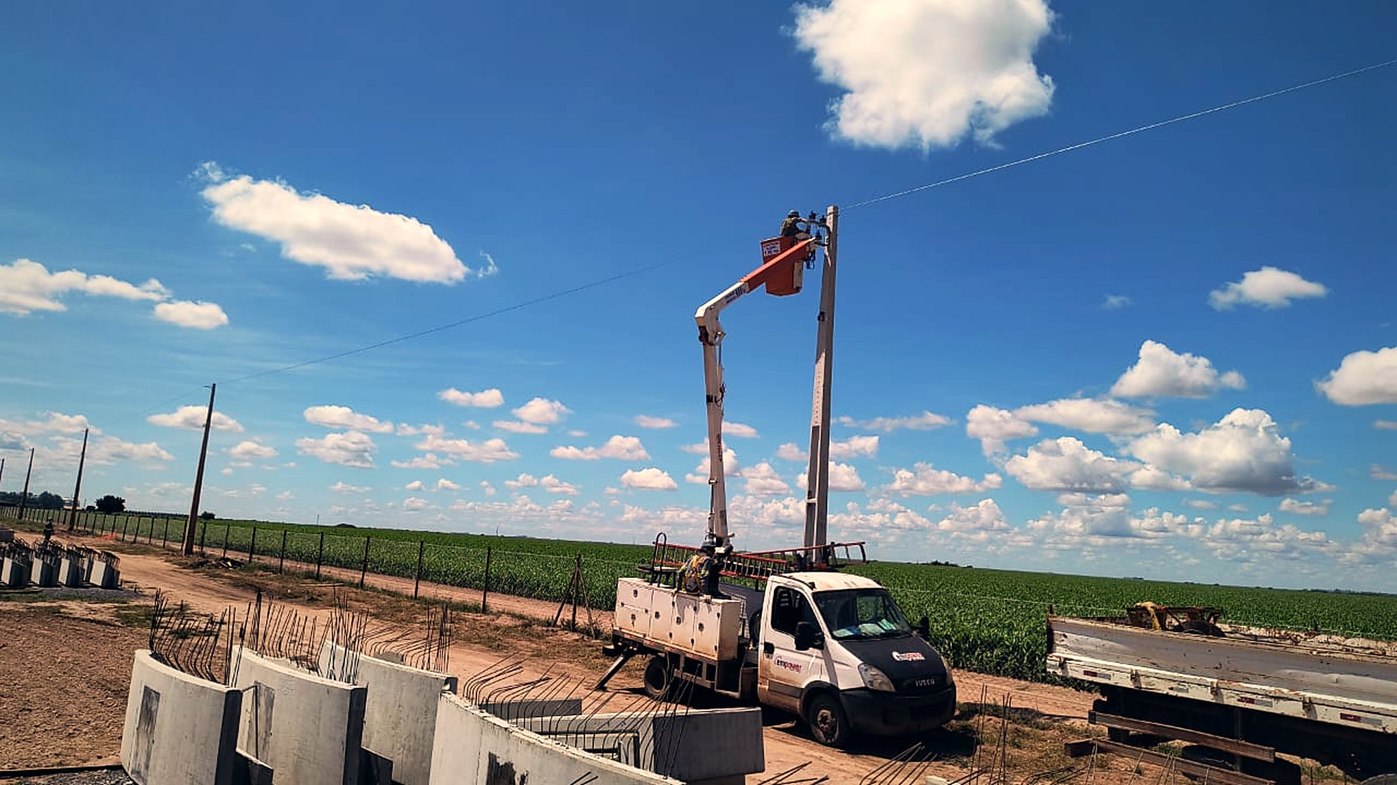Caminhão com munck posicionando poste de concreto em área de implantação industrial sob céu aberto