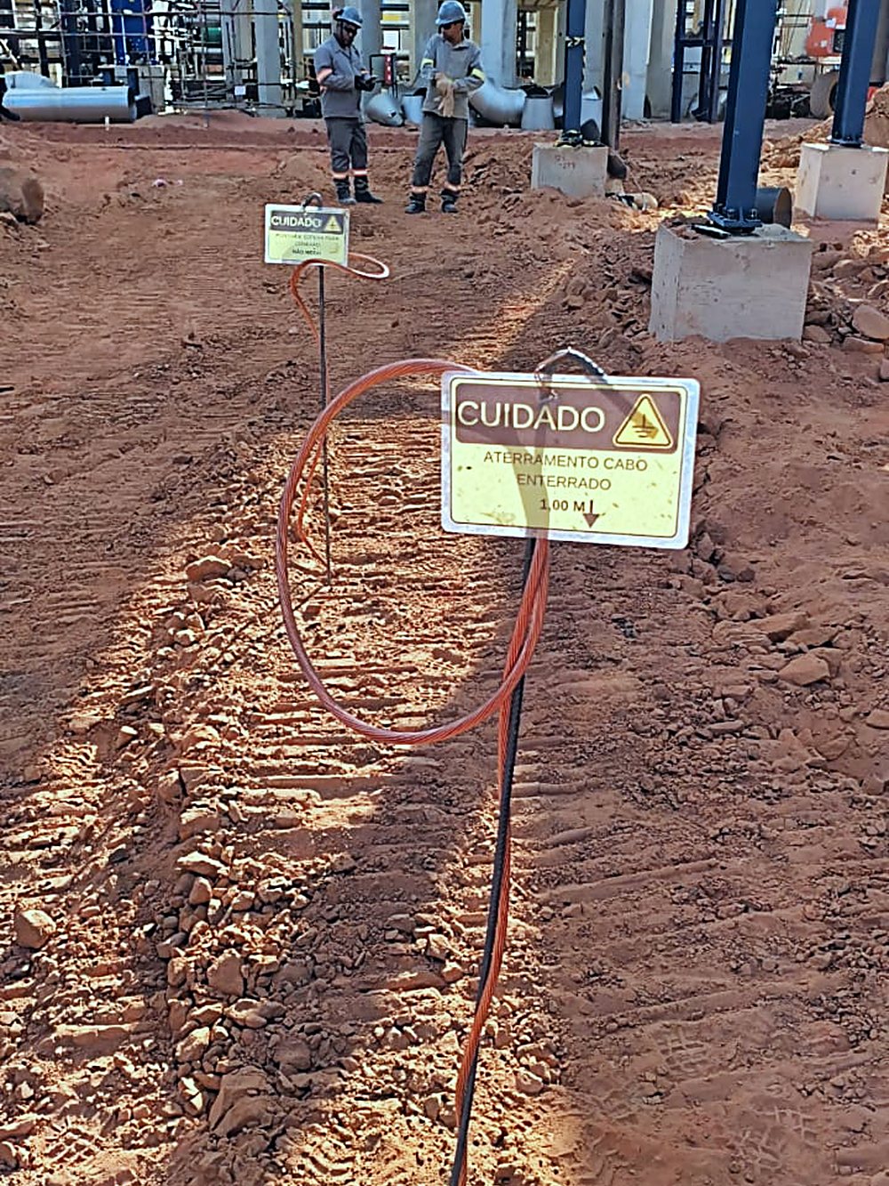 Vala aberta em solo vermelho para passagem de rede subterrânea dentro da planta industrial