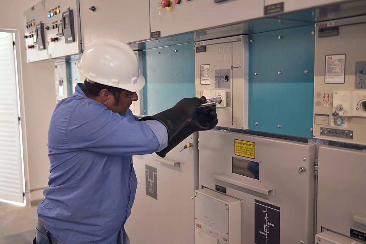 Eletricista com luva isolante opera painel de média tensão durante aferição