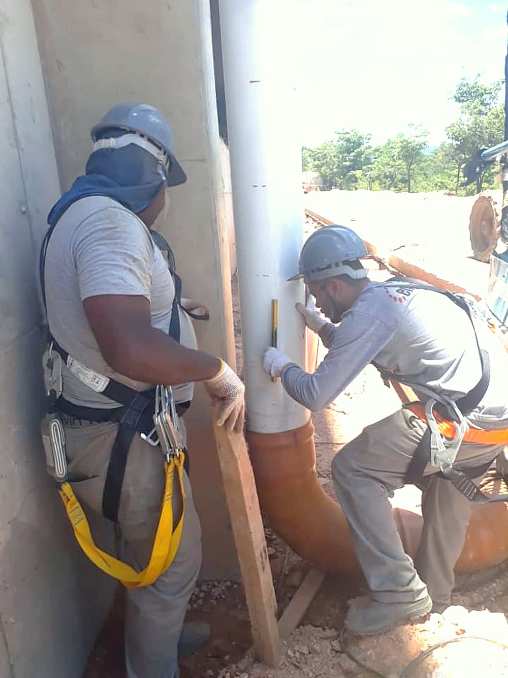 Dois profissionais com cinto de segurança executam serviço junto a pilar de concreto